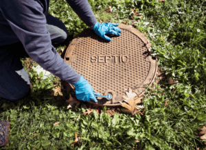 Person opening up a drain in Washington State, specifically in Pierce and King County, illustrating common septic problems and maintenance tips. This image captures the hands-on approach required to address septic system issues, emphasizing the importance of regular inspections and timely interventions. It highlights potential problems such as blockages, leaks, and buildup, stressing the need for proactive care to maintain system health. Against a backdrop of a typical residential setting, it underscores practical advice for homeowners to ensure efficient septic system operation. This portrayal reflects the company's commitment to providing expert guidance and reliable solutions for maintaining healthy septic systems in the local community.